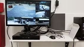 Security camera monitor displaying four views on a desk with mouse, DVR, and computer tower.