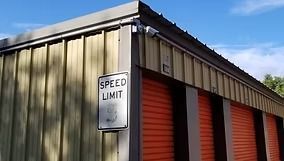 Storage units with orange doors, a speed limit sign, and a blue sky.