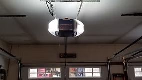 Garage door opener mounted on the ceiling, above a closed garage door.