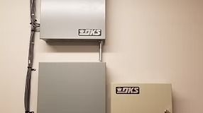 Three gray and tan DKS-branded electrical boxes mounted on a beige wall.