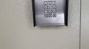 A keypad with numbers 0-9 on a light beige wall.