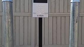 Gray gate with keypad on a black pole, flanked by two silver poles.