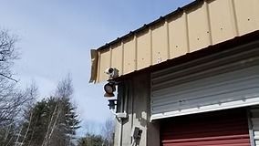 Brown building with a security camera and a partially open red garage door.