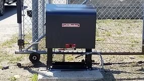 Black LiftMaster gate opener on a concrete base next to a chain-link fence and a gate.