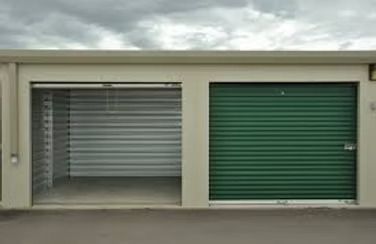 Two storage units; one open, gray interior; the other closed, green door. Outdoor, cloudy sky.