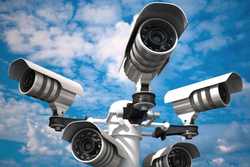 Security cameras on a pole against a blue sky with clouds.