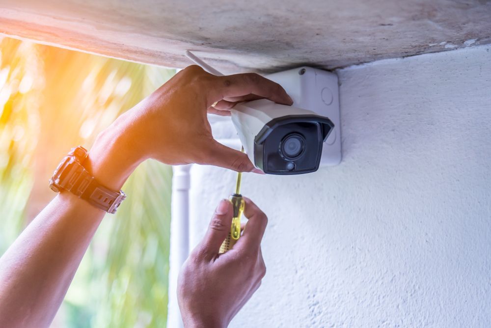 A person installing a security camera on a white building exterior.