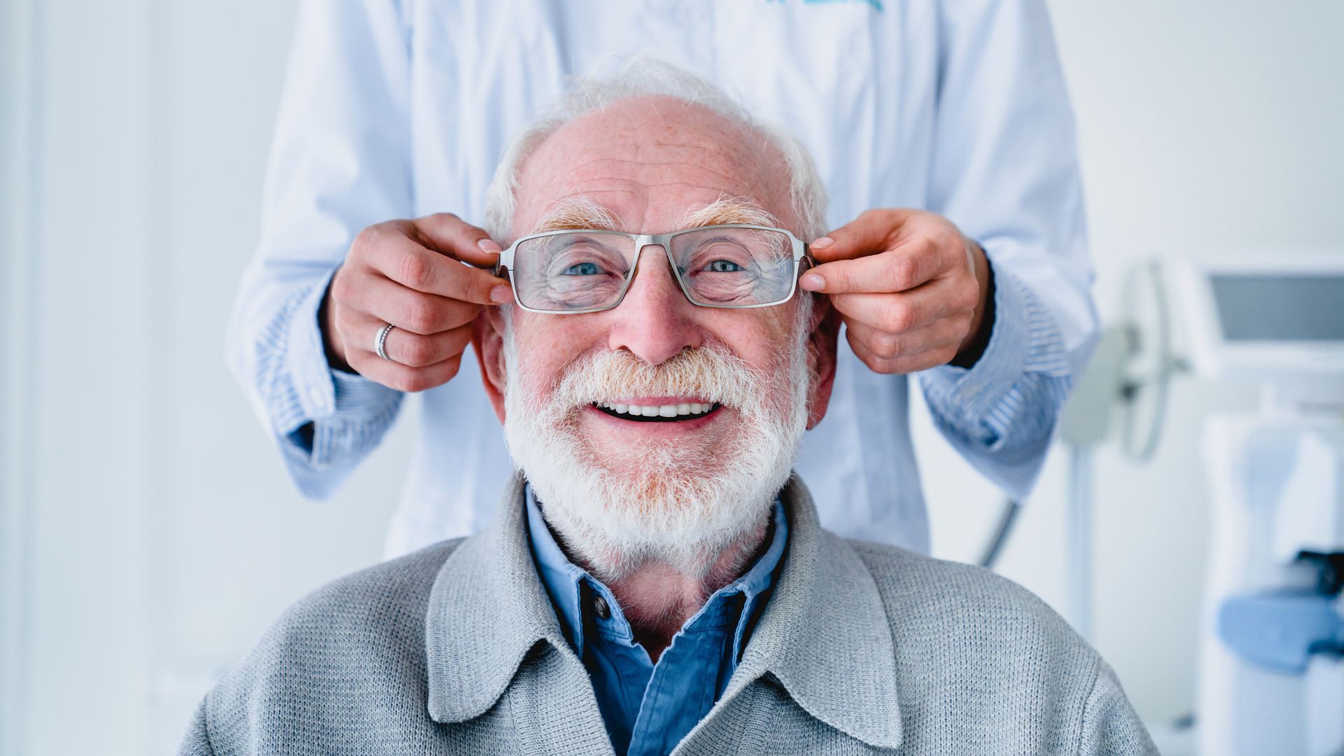 Doctor adjusting eyeglasses on a smiling elderly patient in an exam room.