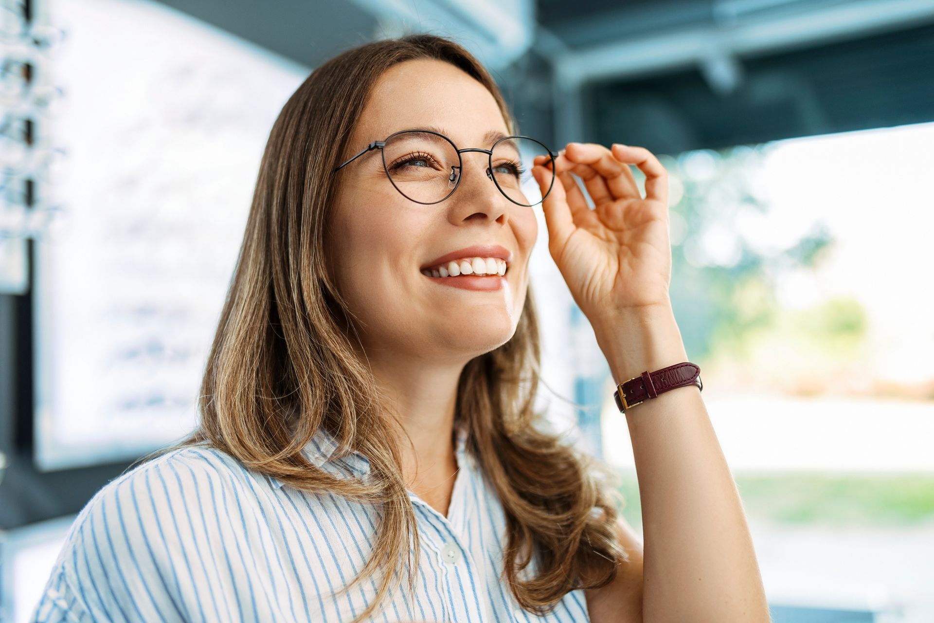 Woman smiles, adjusting round eyeglasses in an optical shop.