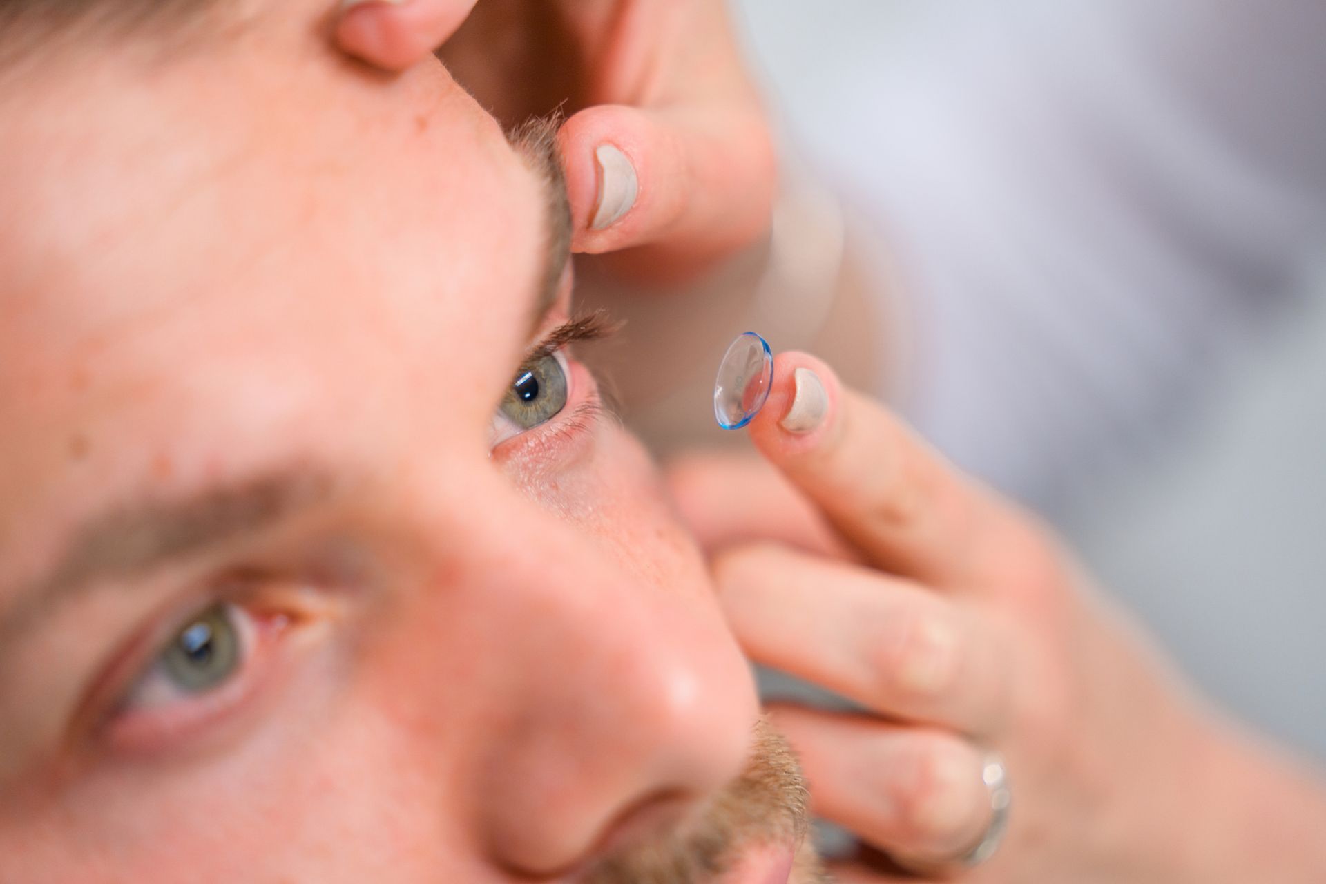 Person receiving a contact lens insertion in their eye. Close-up with focus on eye and hand.