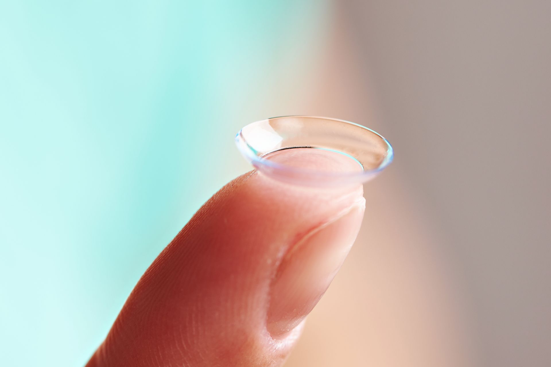 Contact lens on a fingertip against a soft, blurred background.