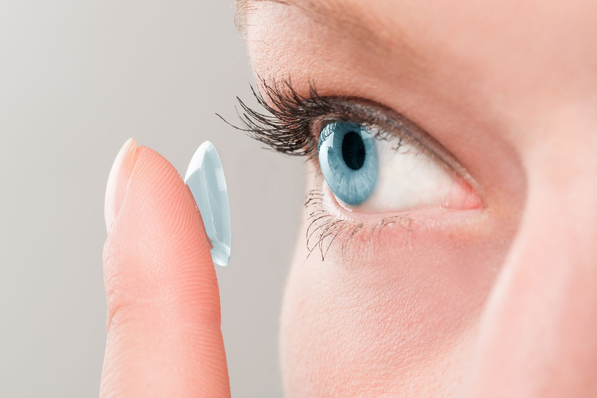 Person's blue eye with a finger holding a contact lens, ready to insert.