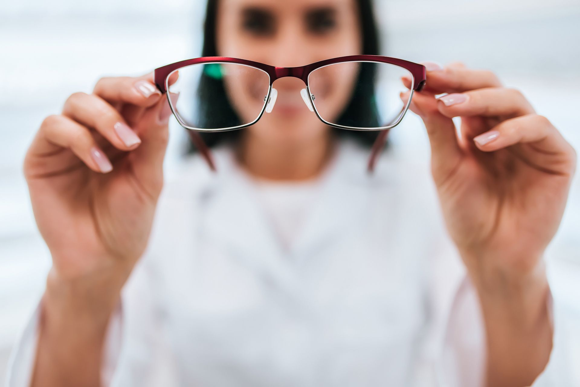 Person holding up eyeglasses, red frames, out of focus.