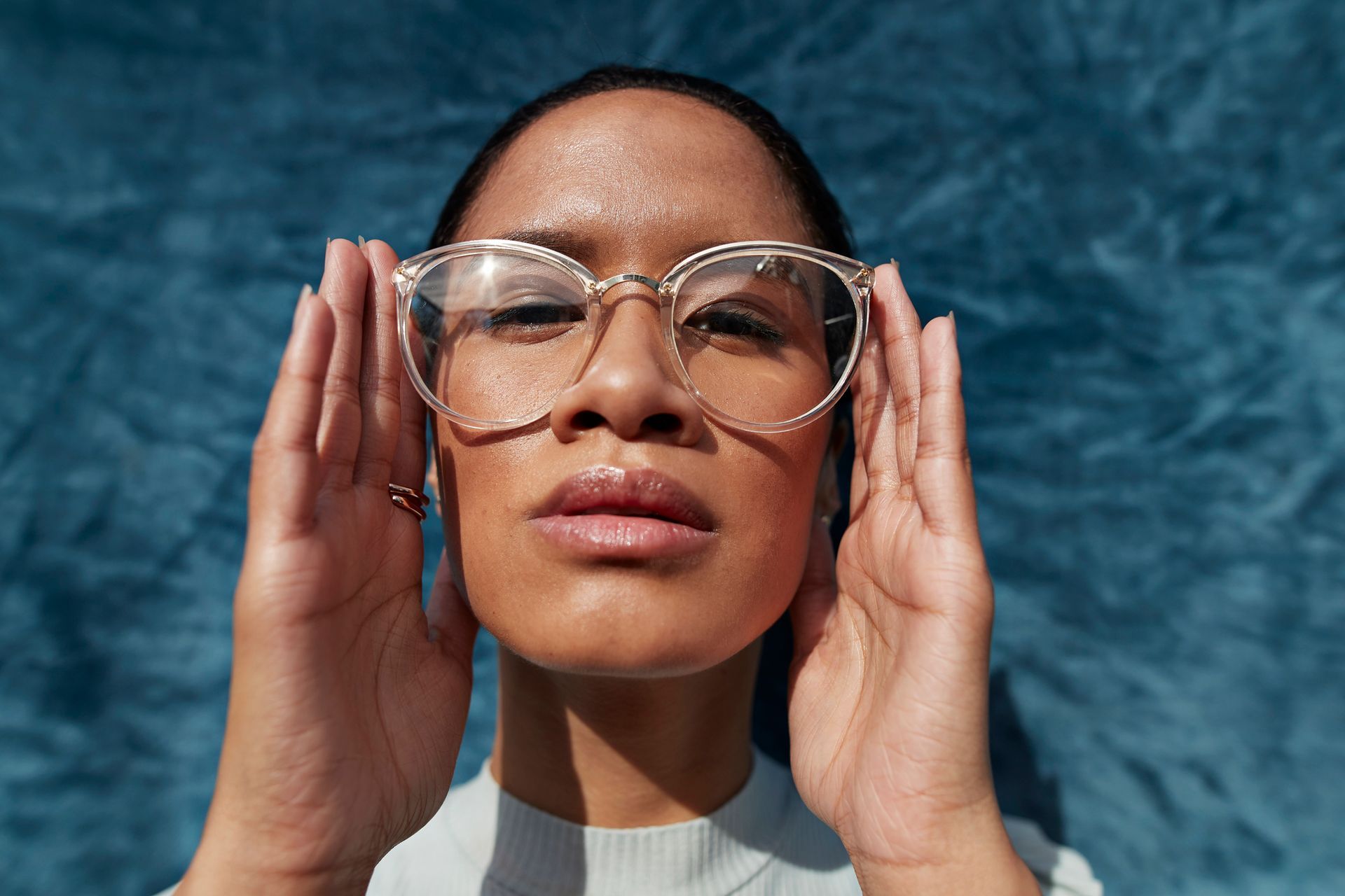 Woman wearing glasses, hands on frames, against a blue textured background.