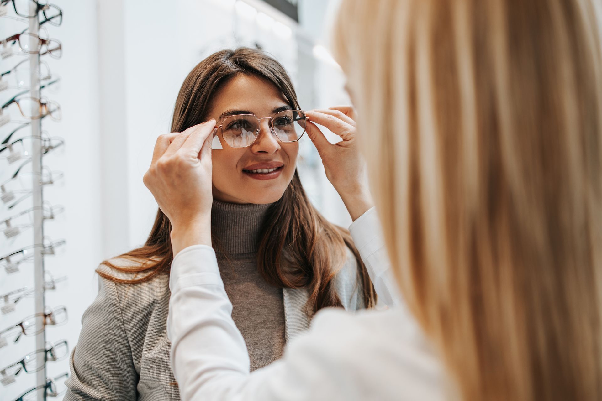 Optician adjusting eyeglasses on a woman in an eyewear store.