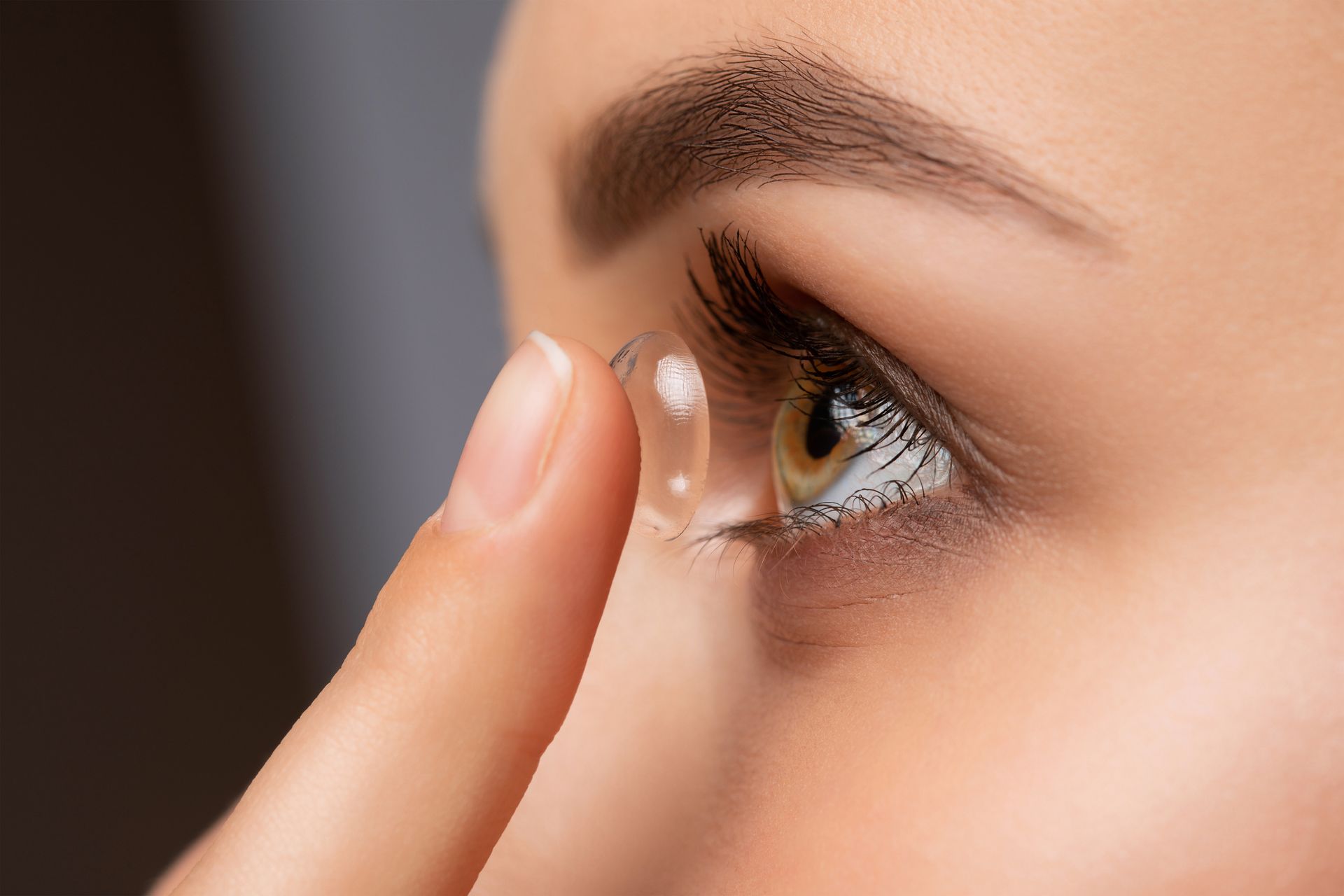 Person inserting a contact lens into their eye. Close-up with focus on eye, finger holding lens.