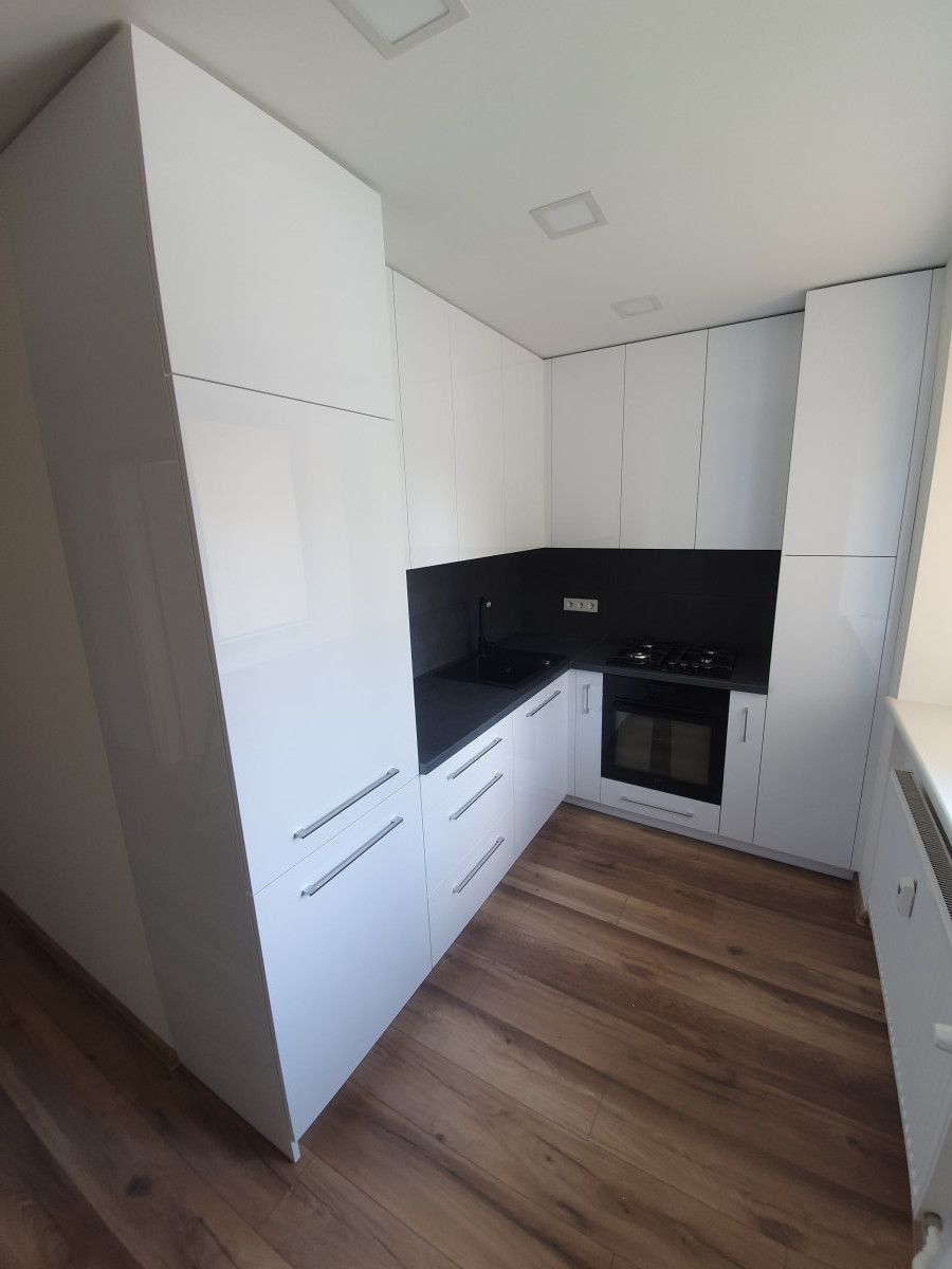 Virtuvė su baltomis spintelėmis ir medinėmis grindimis