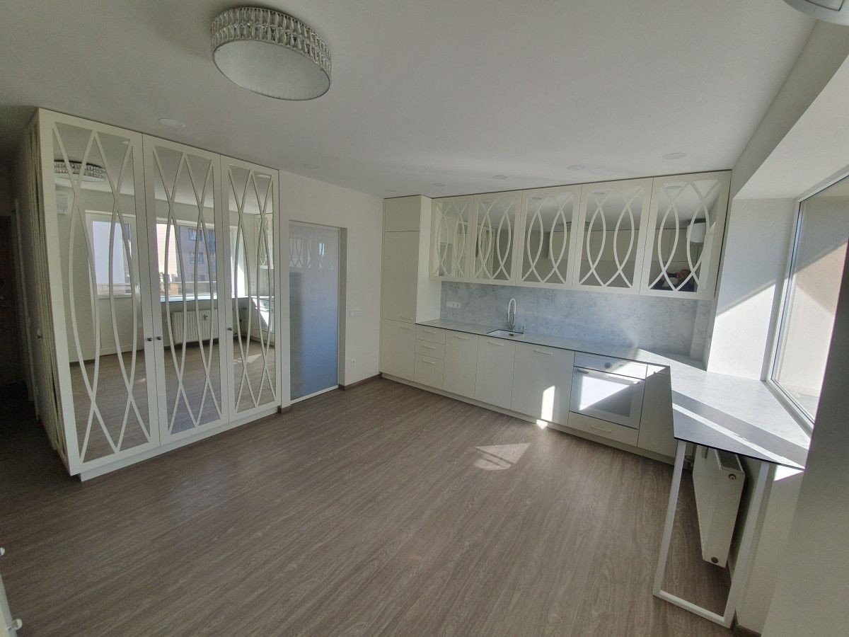 Svetainė su daugybe veidrodžių ant sienų ir virtuve fone.