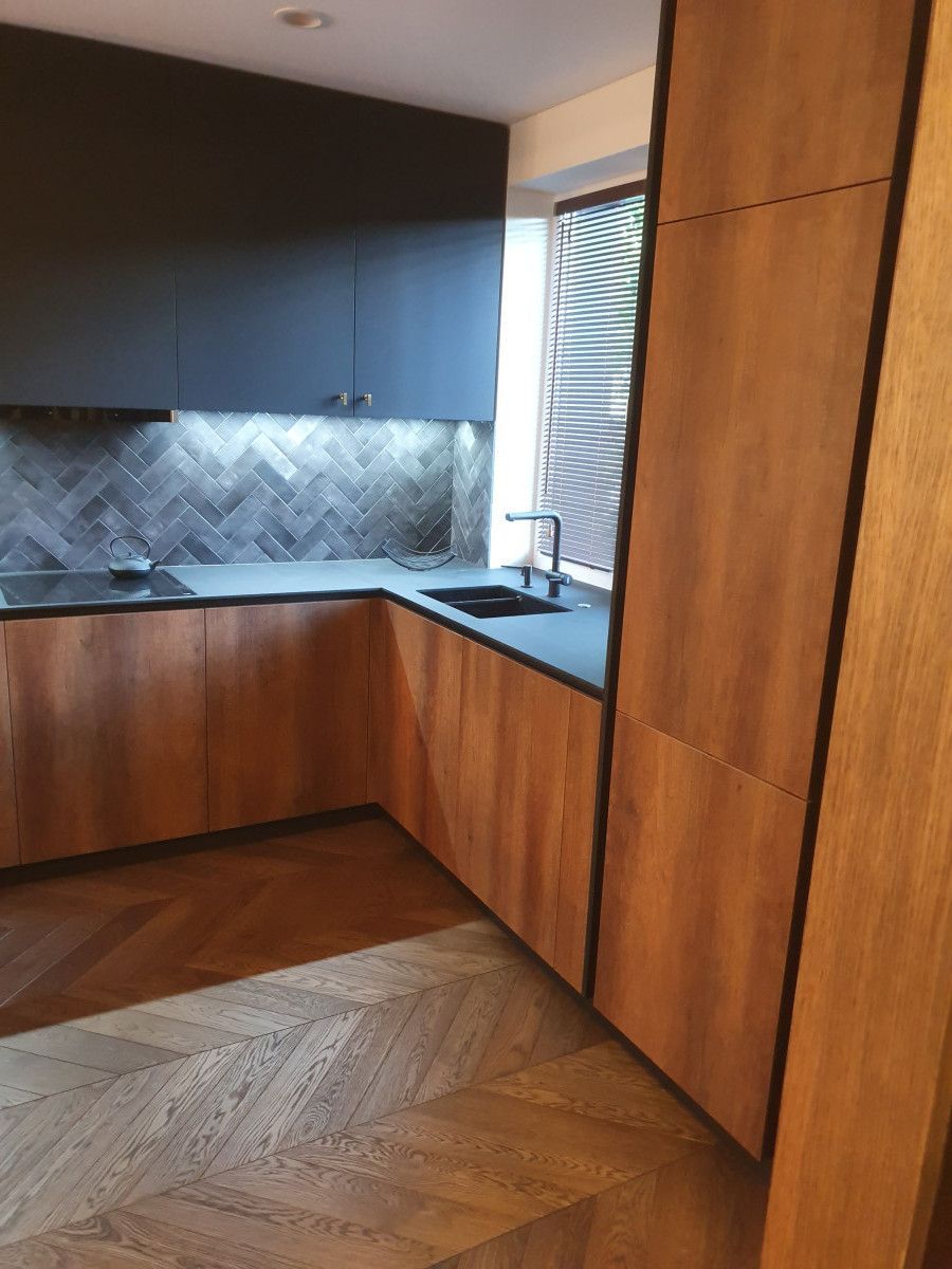 Virtuvė su medinėmis spintelėmis ir juodais stalviršiais