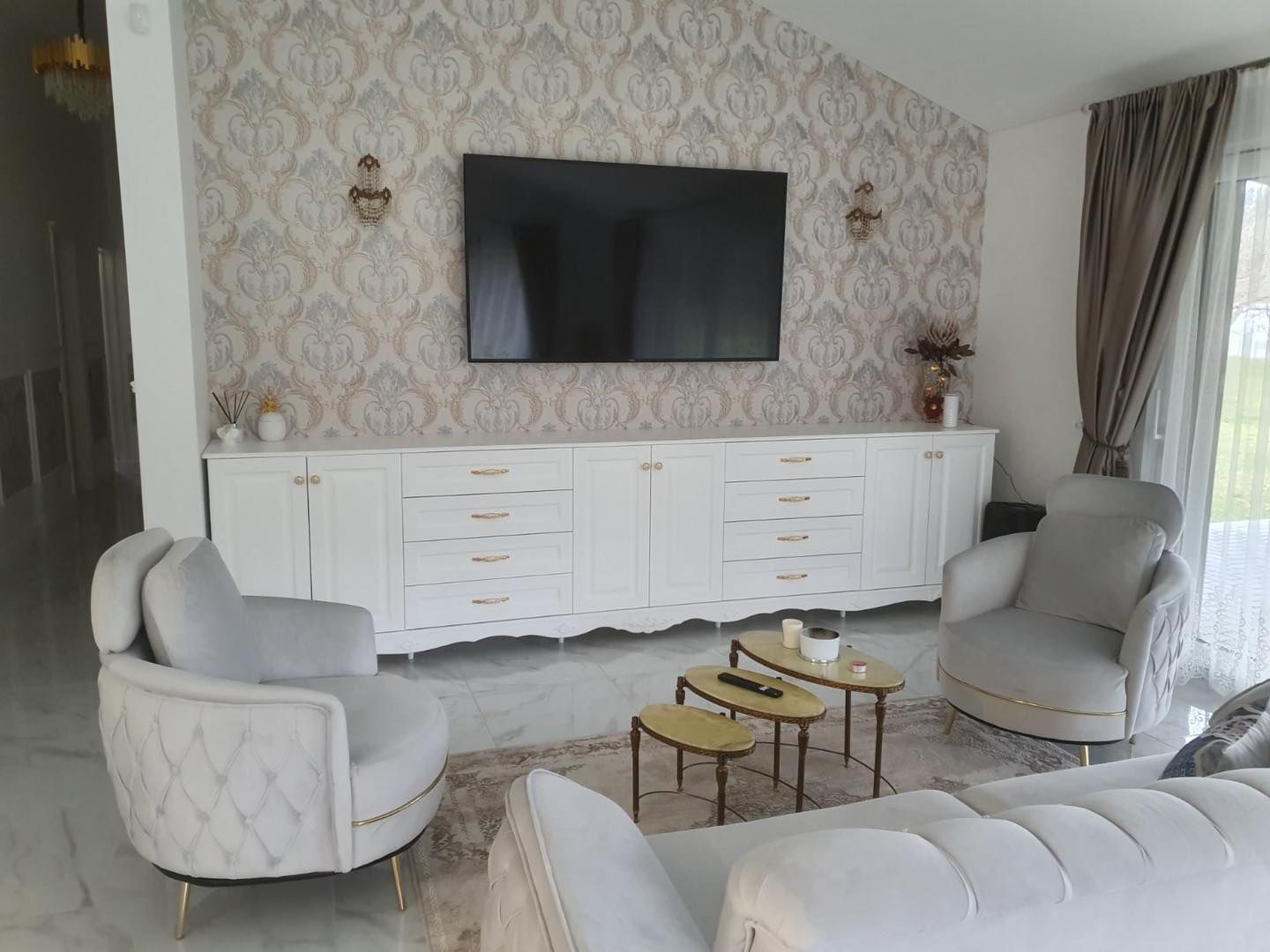 Svetainė su sofa, foteliais, stalais ir plokščiaekraniu televizoriumi.