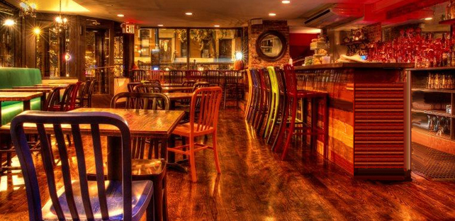 Interior of a dimly lit bar with wooden tables, chairs, and a bar counter.