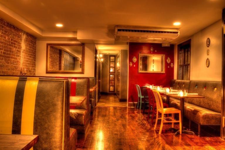 Restaurant interior with booths, tables, and a hallway. Exposed brick, red wall, warm lighting.