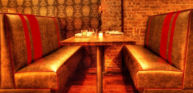 A restaurant booth with a red-striped back, table, and brick and skull-print background.