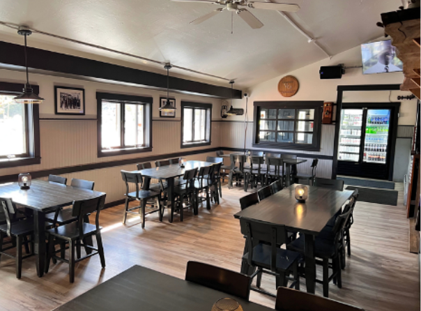 Interior of a restaurant with wooden tables and chairs, windows, and decorative items.