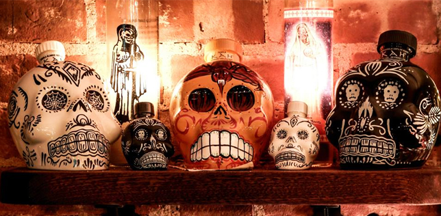 Shelves of skull-shaped liquor bottles. Some are decorated with intricate designs. A statue stands between them.
