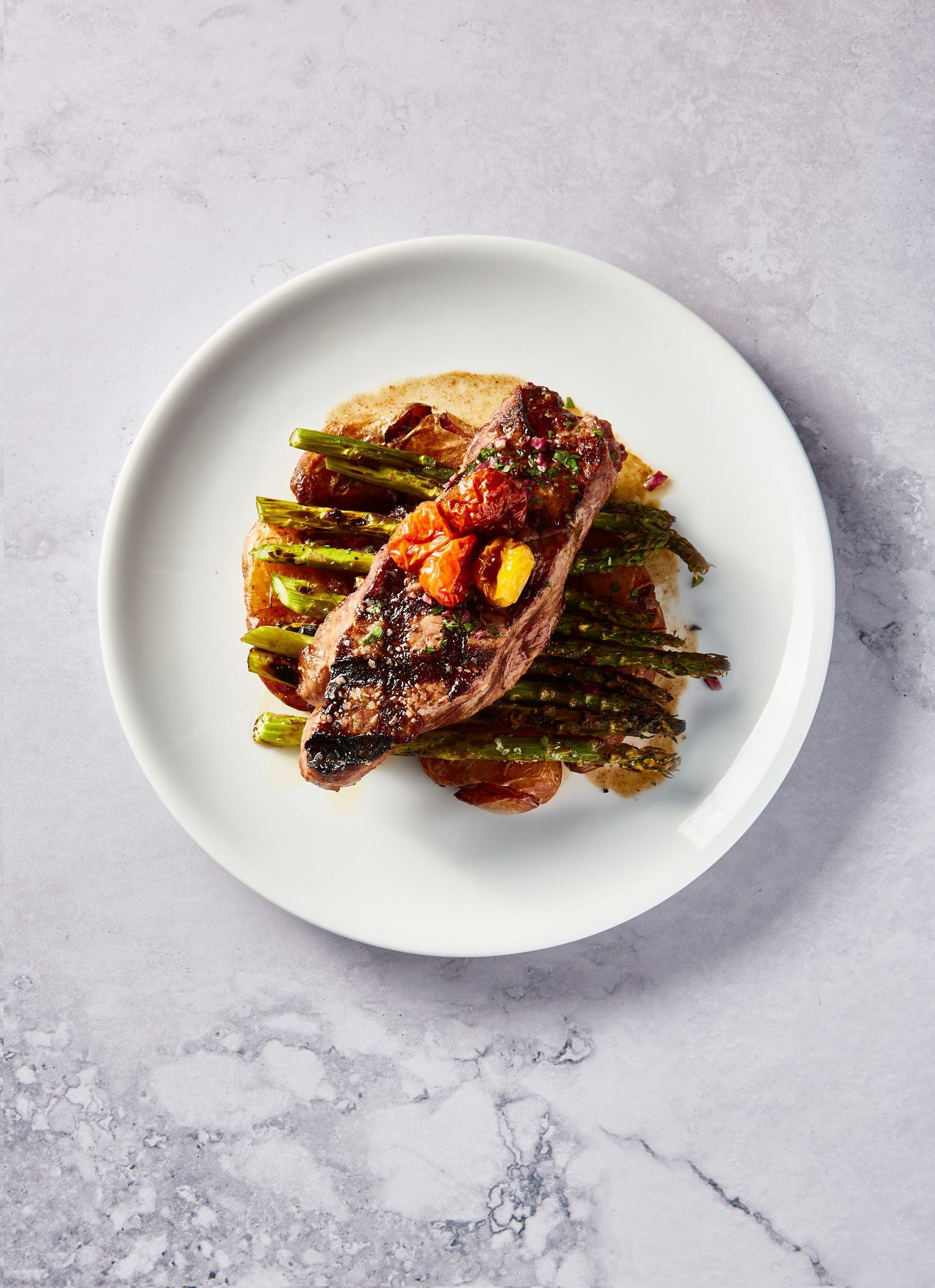 Steak with tomato salsa on a bed of asparagus and potatoes on a white plate.