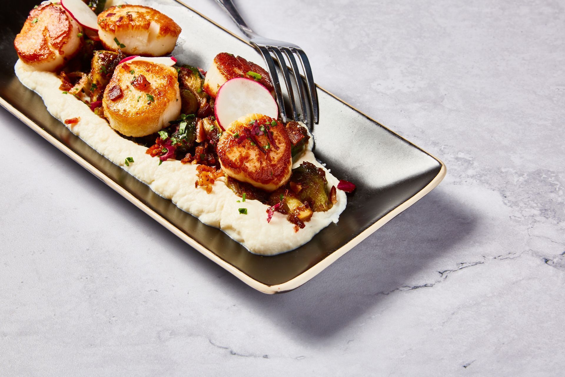 Seared scallops served on a rectangular plate with mashed potatoes, mushrooms, and radish slices.