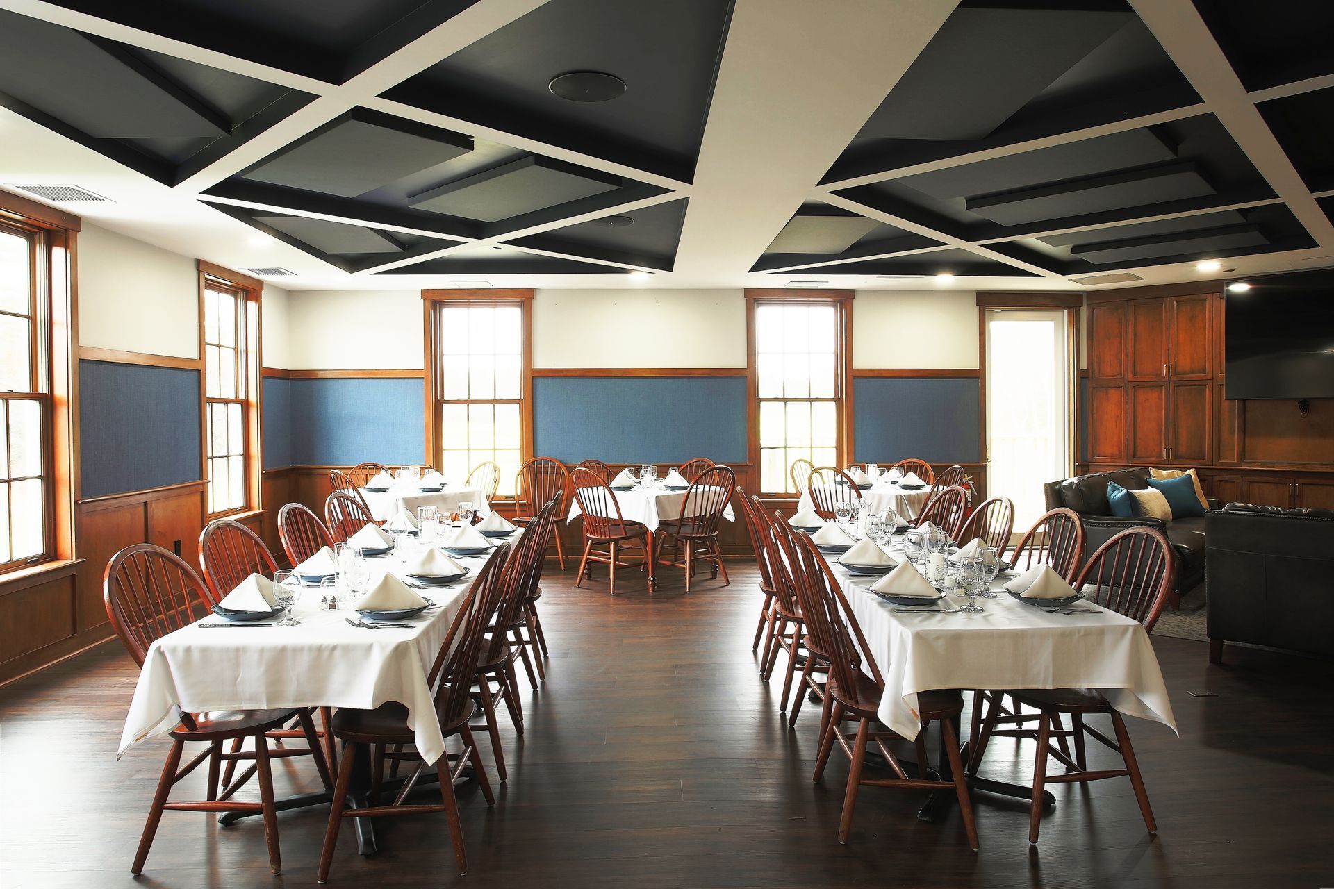 Formal dining room with long tables set for a meal. Dark wood floor, walls, and ceiling with geometric design.
