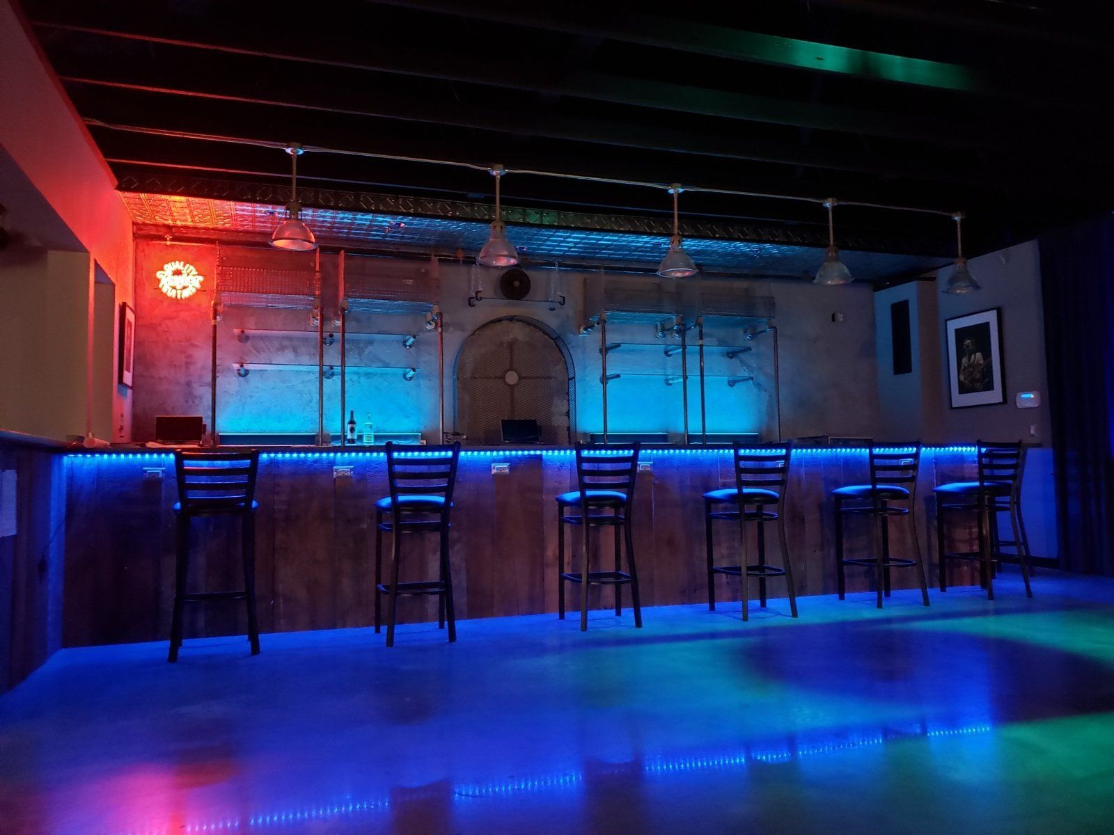 Bar with blue and red lighting, six stools at the counter, a brick wall, and pendant lights.