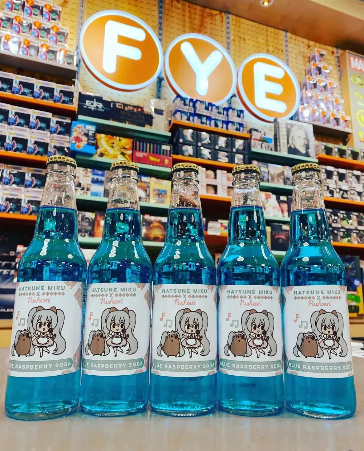 Five blue soda bottles with Pusheen labels, in front of an FYE store sign.