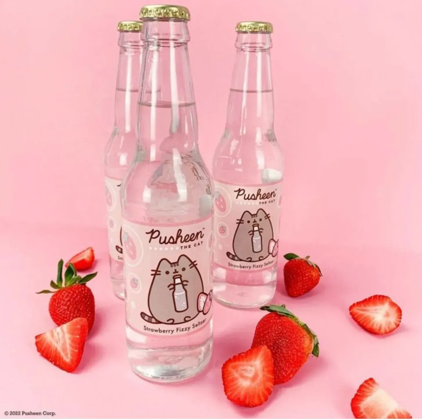 Three bottles of Pusheen strawberry soda with strawberries on a pink background.