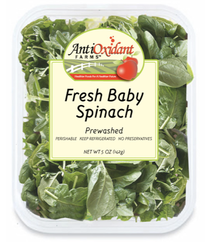 Fresh baby spinach in a plastic container with a label that says