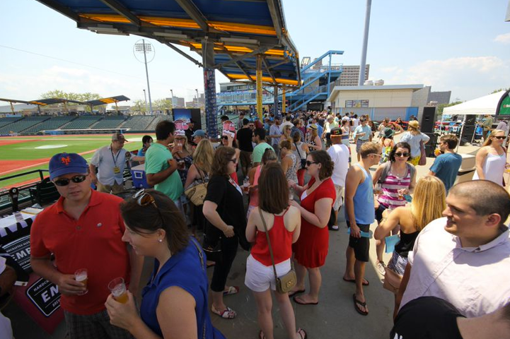People gather outdoors at a stadium under a blue and yellow canopy.