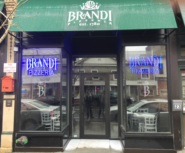 Brandi Pizzeria storefront with a green awning and neon signs.