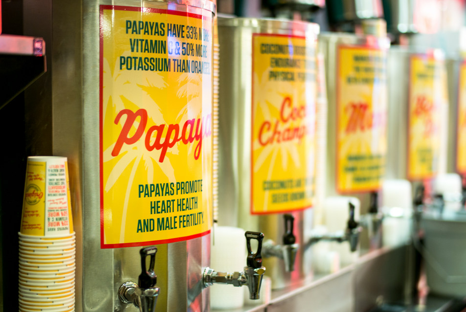 Row of juice dispensers with yellow labels: Papaya, Cool Change, and Mango.