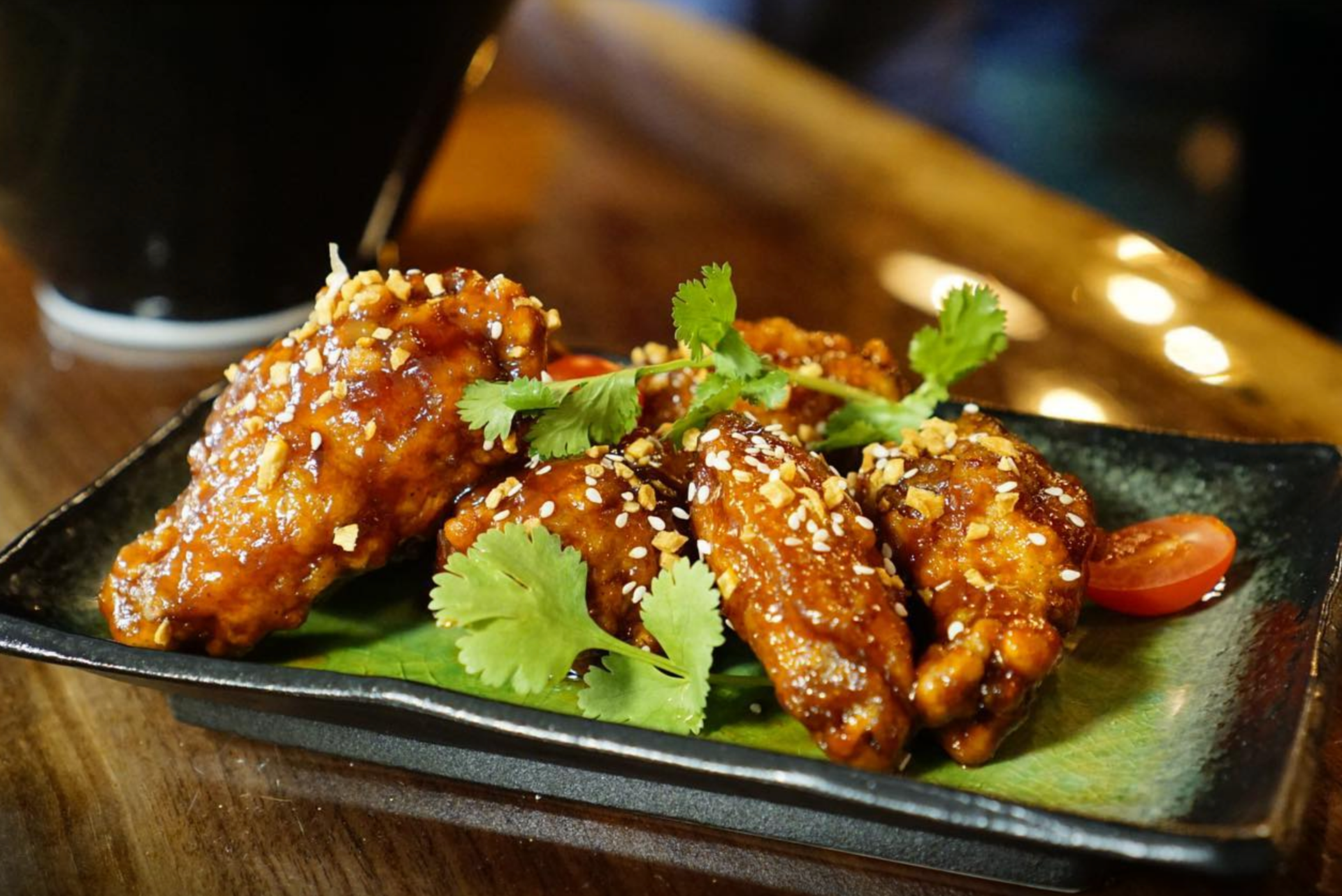 Chicken wings with sauce, garnished with cilantro and sesame seeds on a plate.