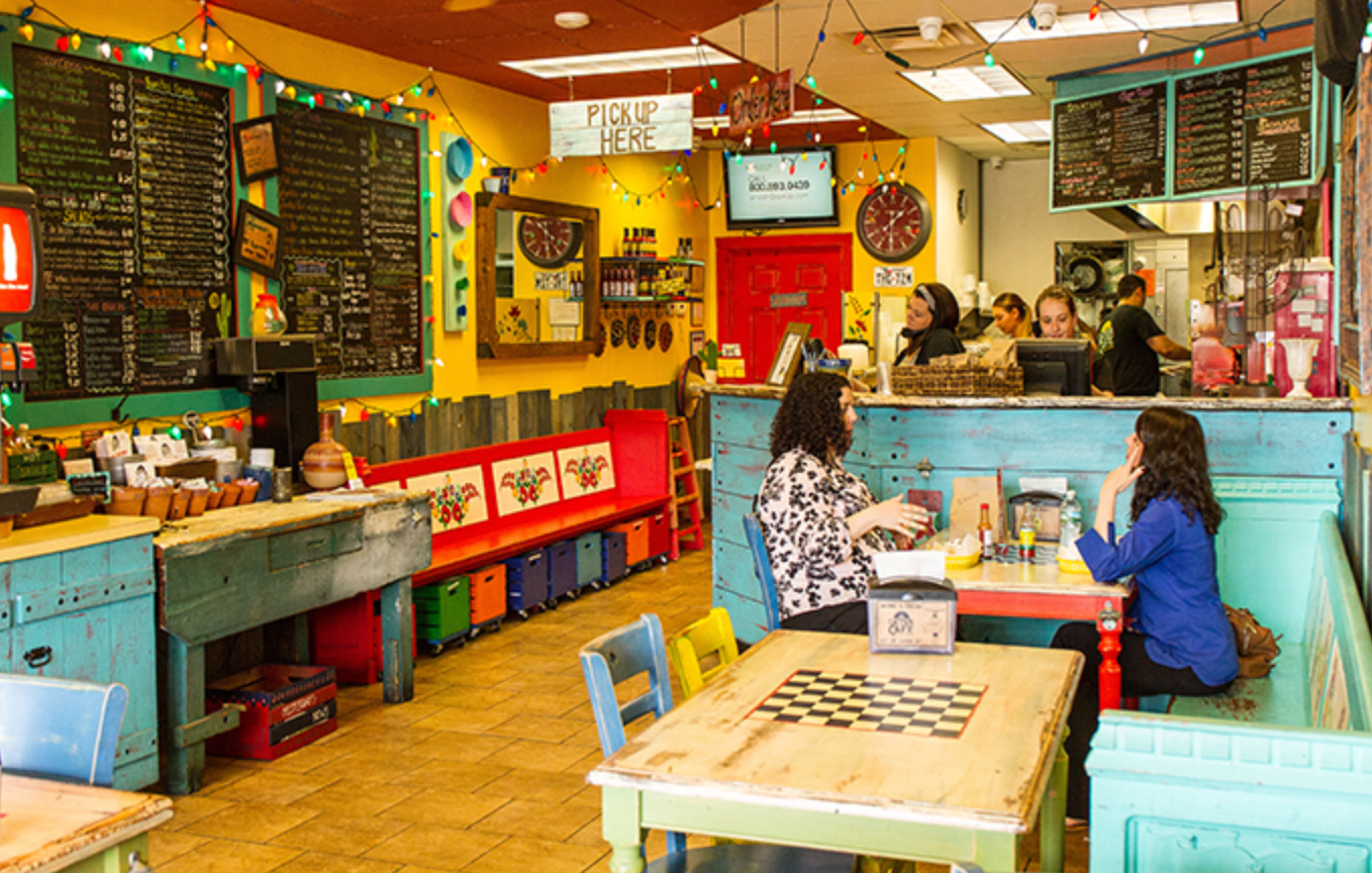 Colorful Mexican restaurant interior: customers at tables, counter with staff, menu boards on walls.
