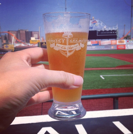 Hand holding a beer glass at a baseball stadium. Glass has