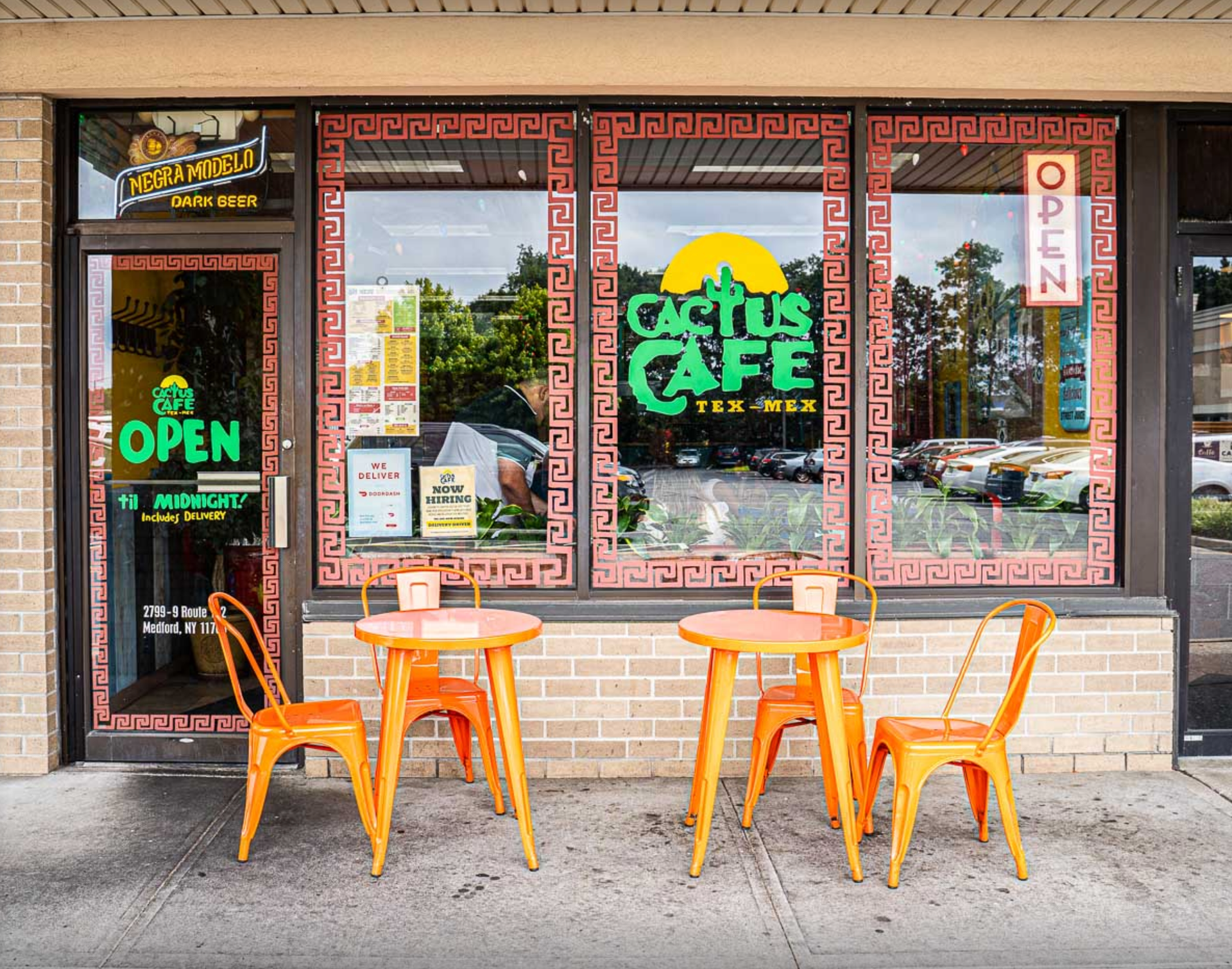 Cactus Cafe storefront with orange tables, chairs. Green logo, open sign. Brick building.