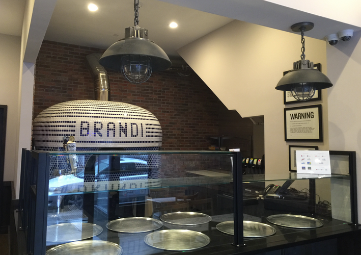 Brandi pizza restaurant interior with brick oven, display case, and pendant lights.