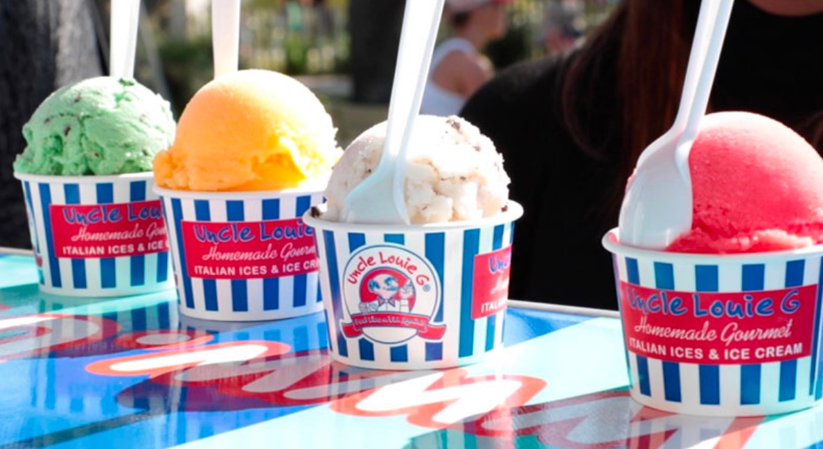 Four cups of colorful ice cream with spoons, on a blue and white striped table.