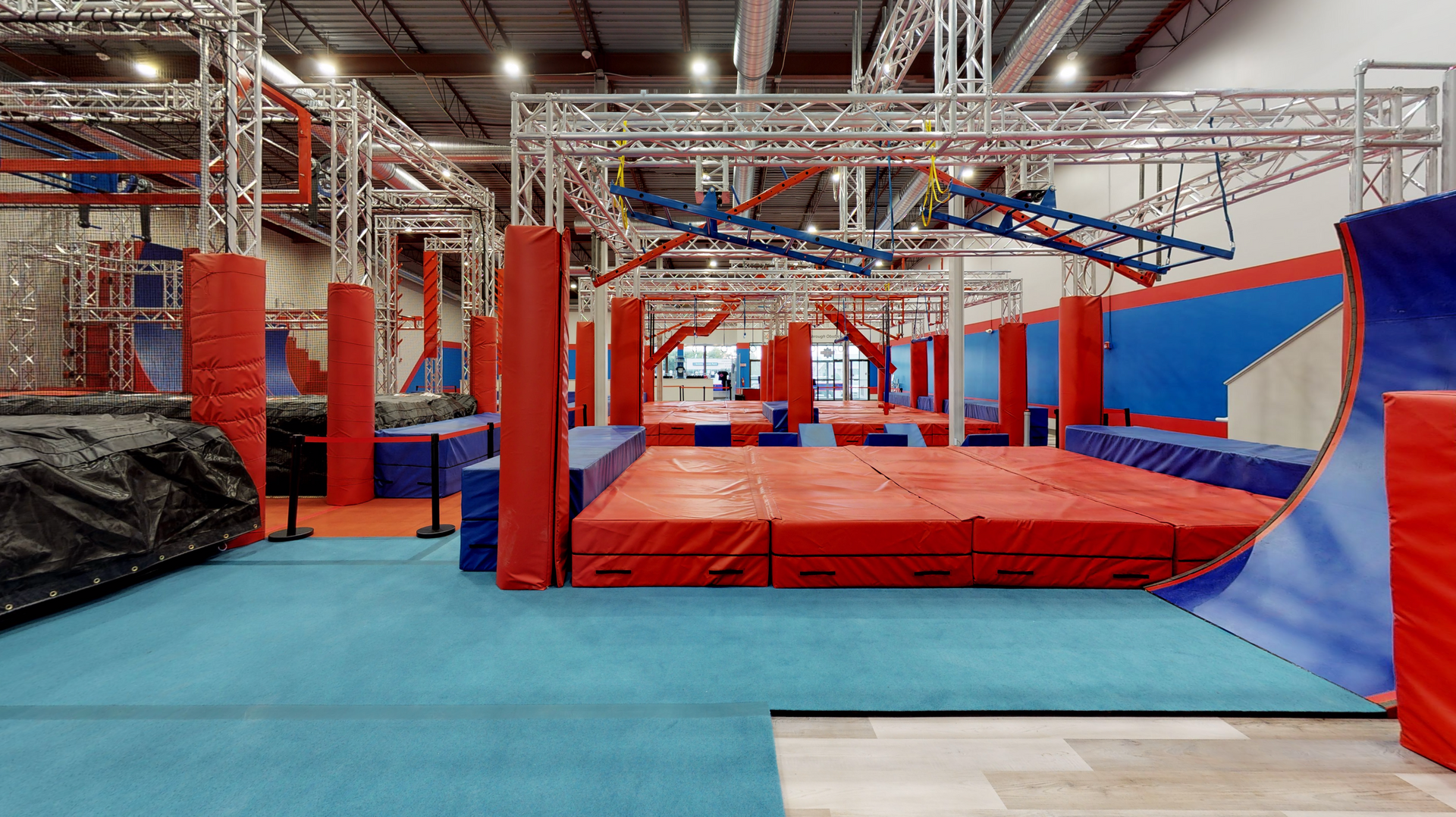 Indoor ninja warrior course with red and blue obstacles and padding.