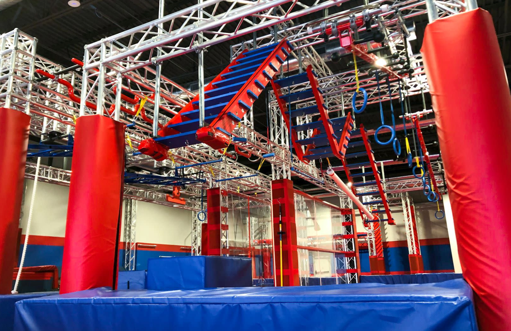 An indoor obstacle course with red and blue elements, metal frames, and padded safety columns.