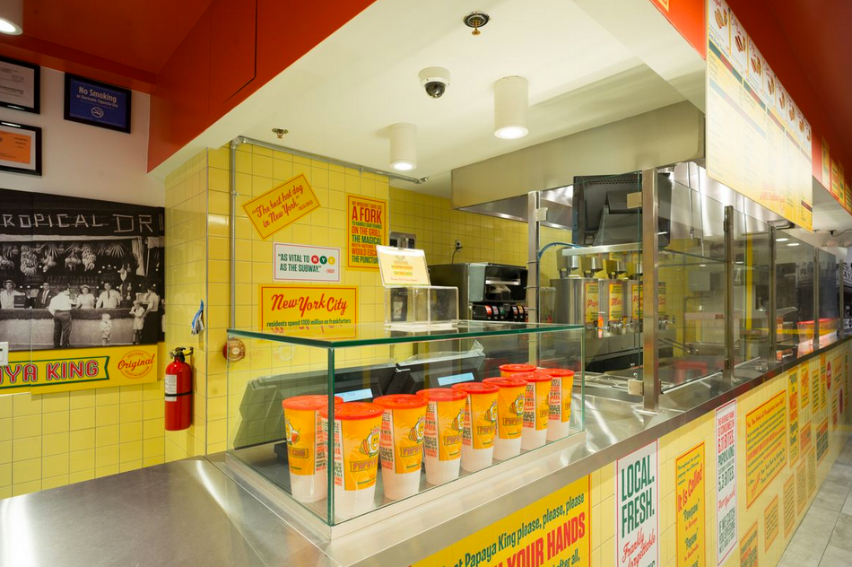 Interior view of a New York City eatery with a bright yellow tiled wall and a stainless steel counter.