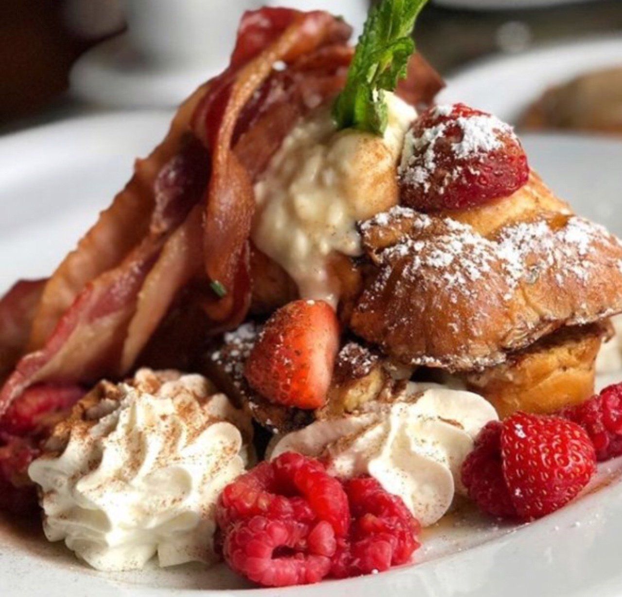 French toast topped with bacon, berries, whipped cream, and mint sprig.