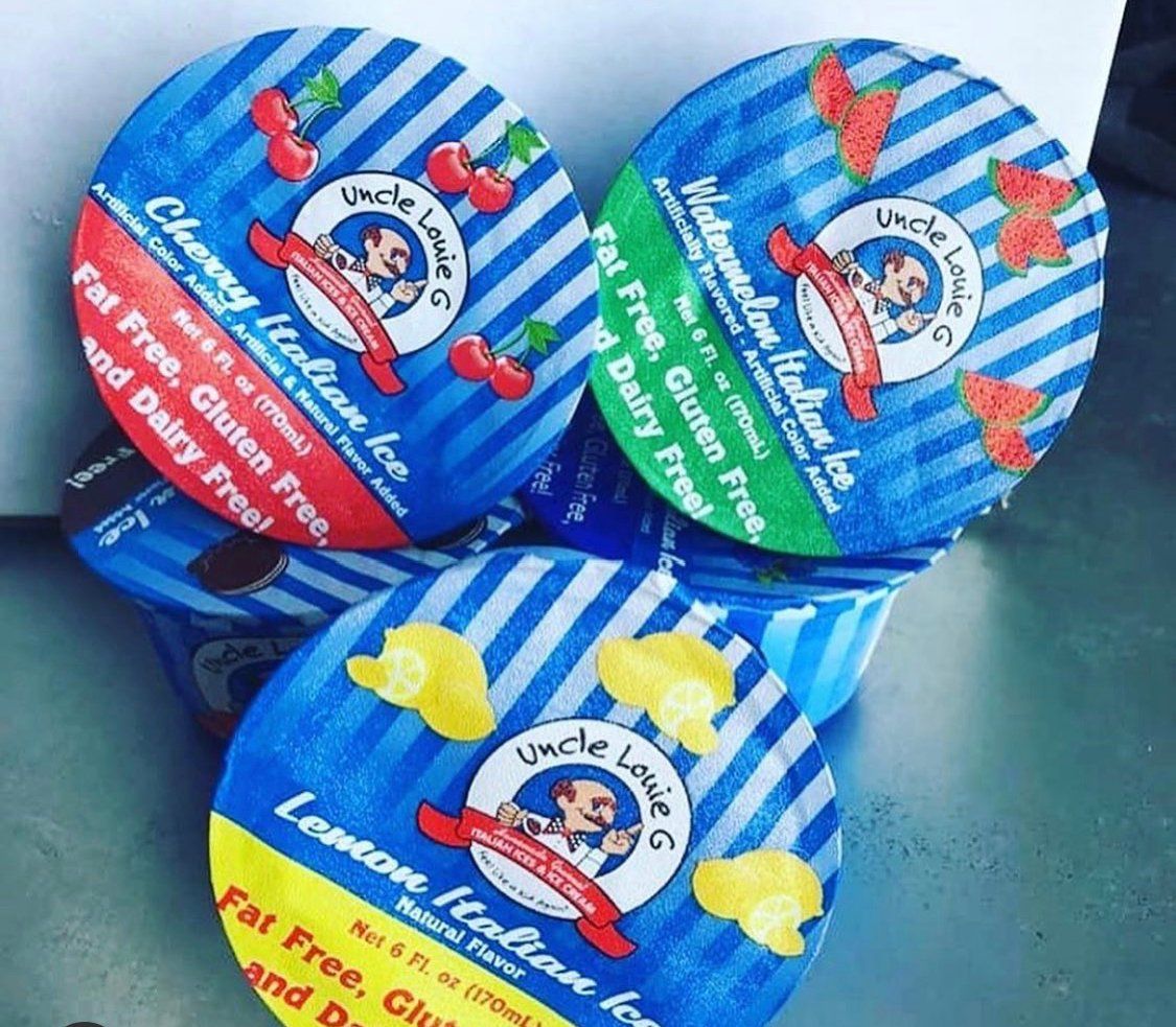 Three Uncle Louie G's Italian ice containers: cherry, watermelon, and lemon flavors, atop blue striped cups.